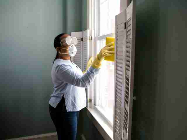 A person wiping window shutters while cleaning.