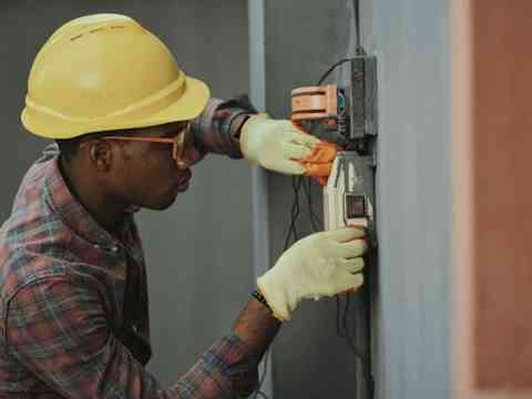 An electrician working on a wall-mounted electrical box.