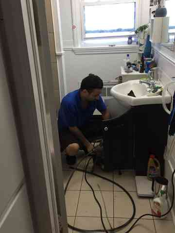 A technician clearing a bathroom sink drain with an auger.
